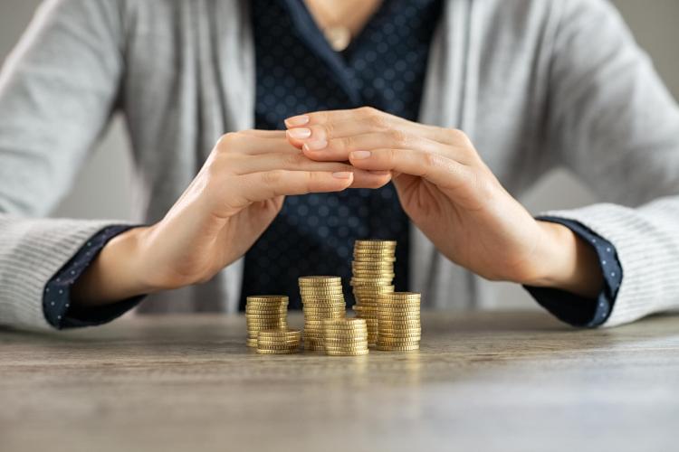 Hands crossed over stacks of gold coins to protect them